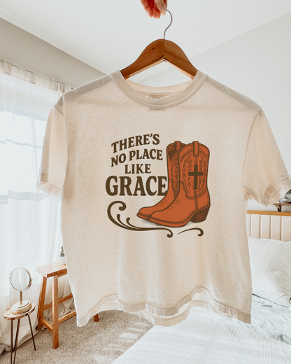 Western Christian t-shirt reading “There’s No Place Like Grace” with cowgirl boots and cross design on Comfort Colors cropped tee.