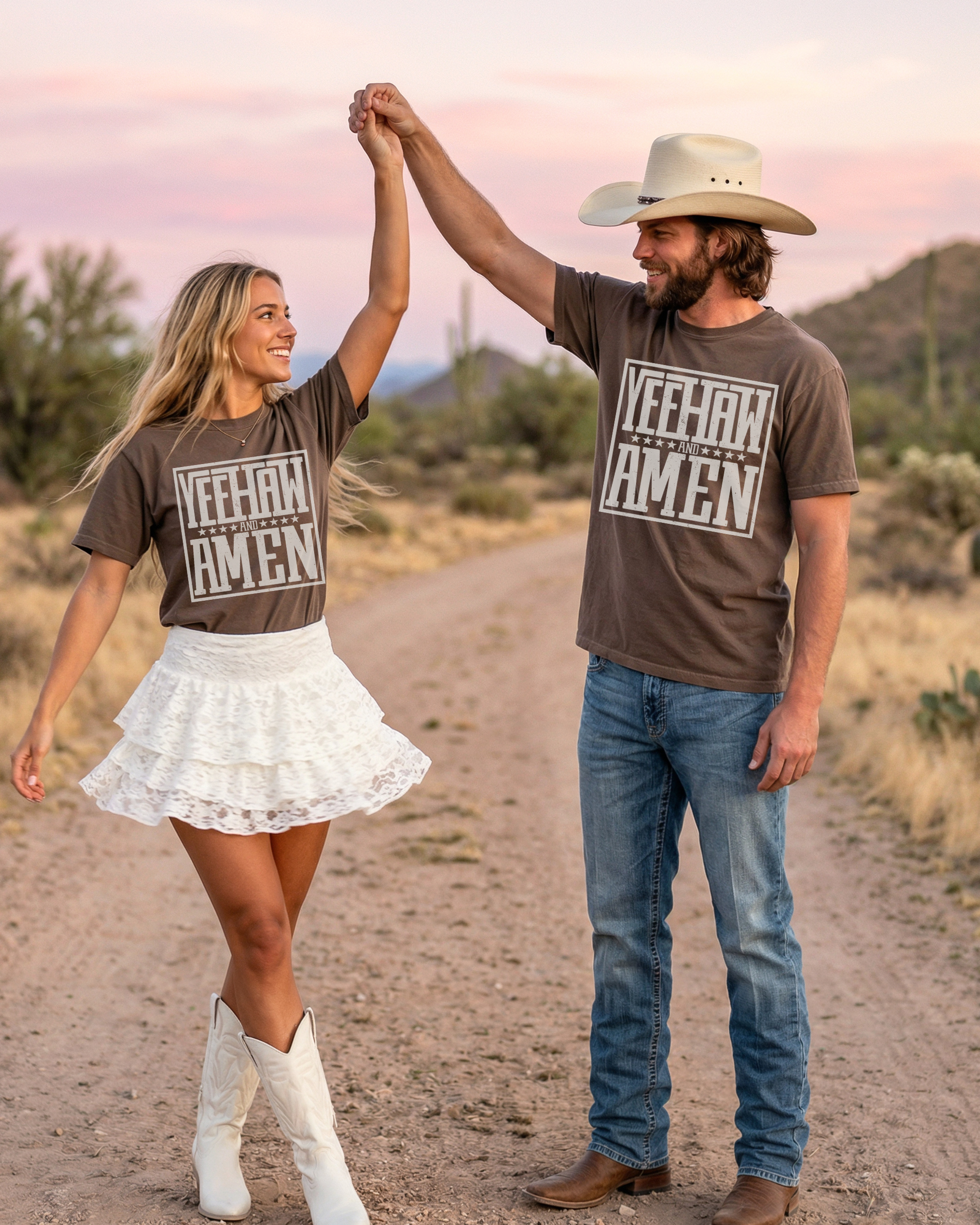 Couple wearing matching Yeehaw and Amen Christian western graphic t-shirts dancing on a desert road at sunset, styled with cowboy boots and denim for a cowgirl and cowboy outfit