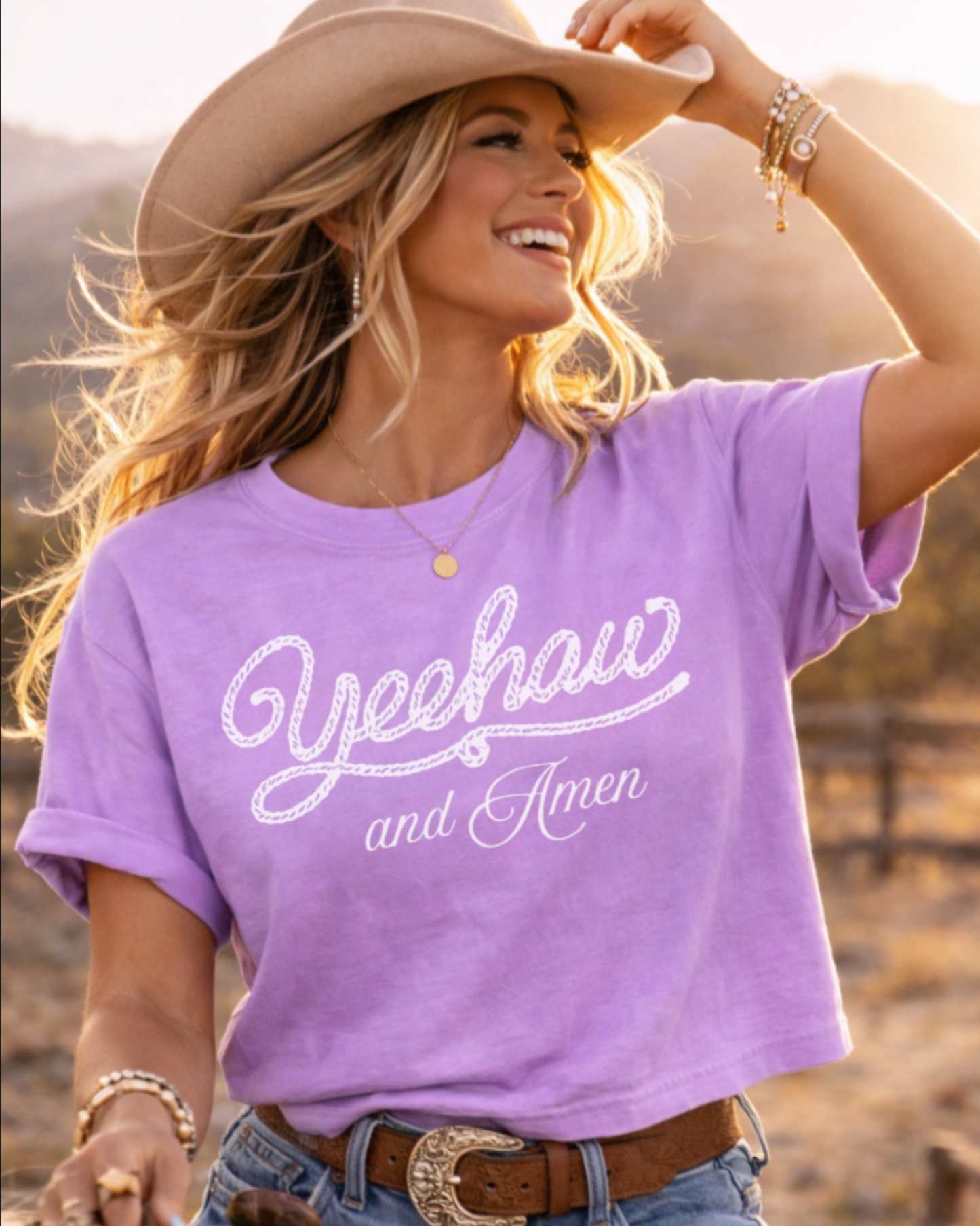 Woman wearing a purple Yeehaw and Amen Comfort Colors western Christian graphic tee, styled in a golden hour ranch setting with cowgirl aesthetic